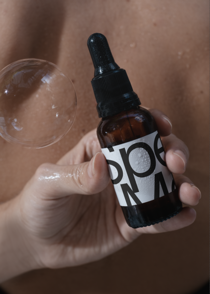 Close-up of a skincare dropper bottle mockup with a bold label held by a hand, with a bubble nearby, ideal for beauty product branding designs.